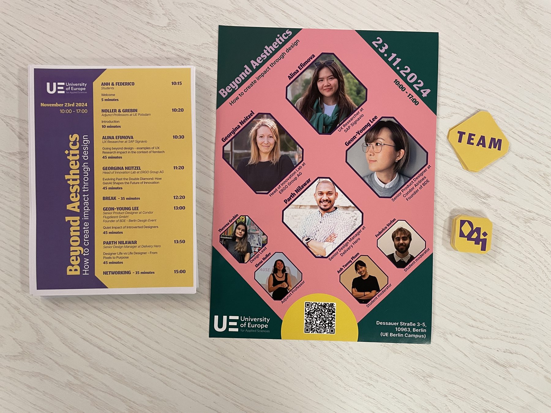 Printed conference materials: the pink and green speaker poster, the purple and yellow timetable handout, and TEAM and D4i stickers