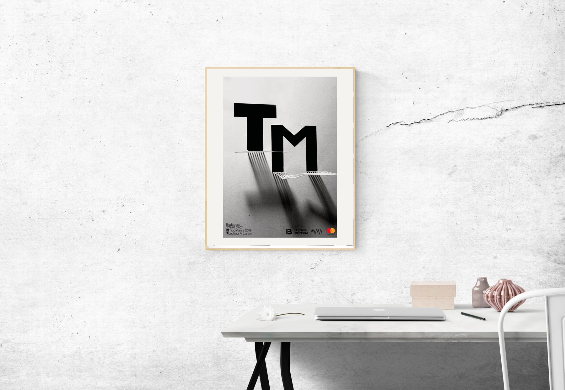 Mockup: the TM poster framed on a white wall above a desk