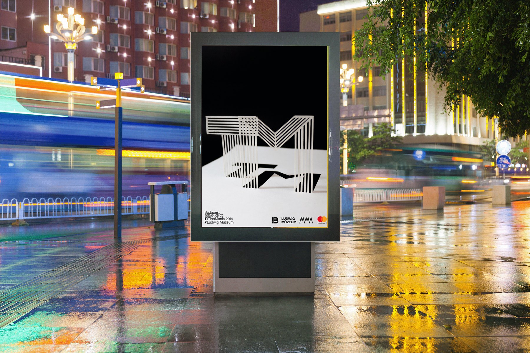 Mockup: the black TipoMánia poster in a backlit street billboard at night